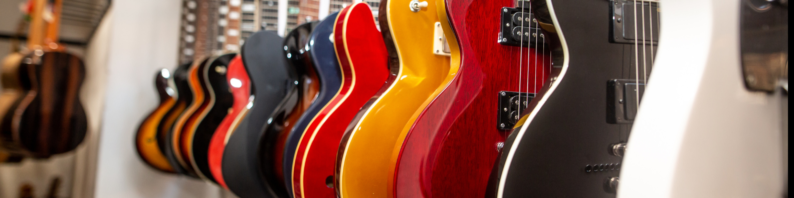 An image showing lots of different guitars in different colours and styles in a guitar shop